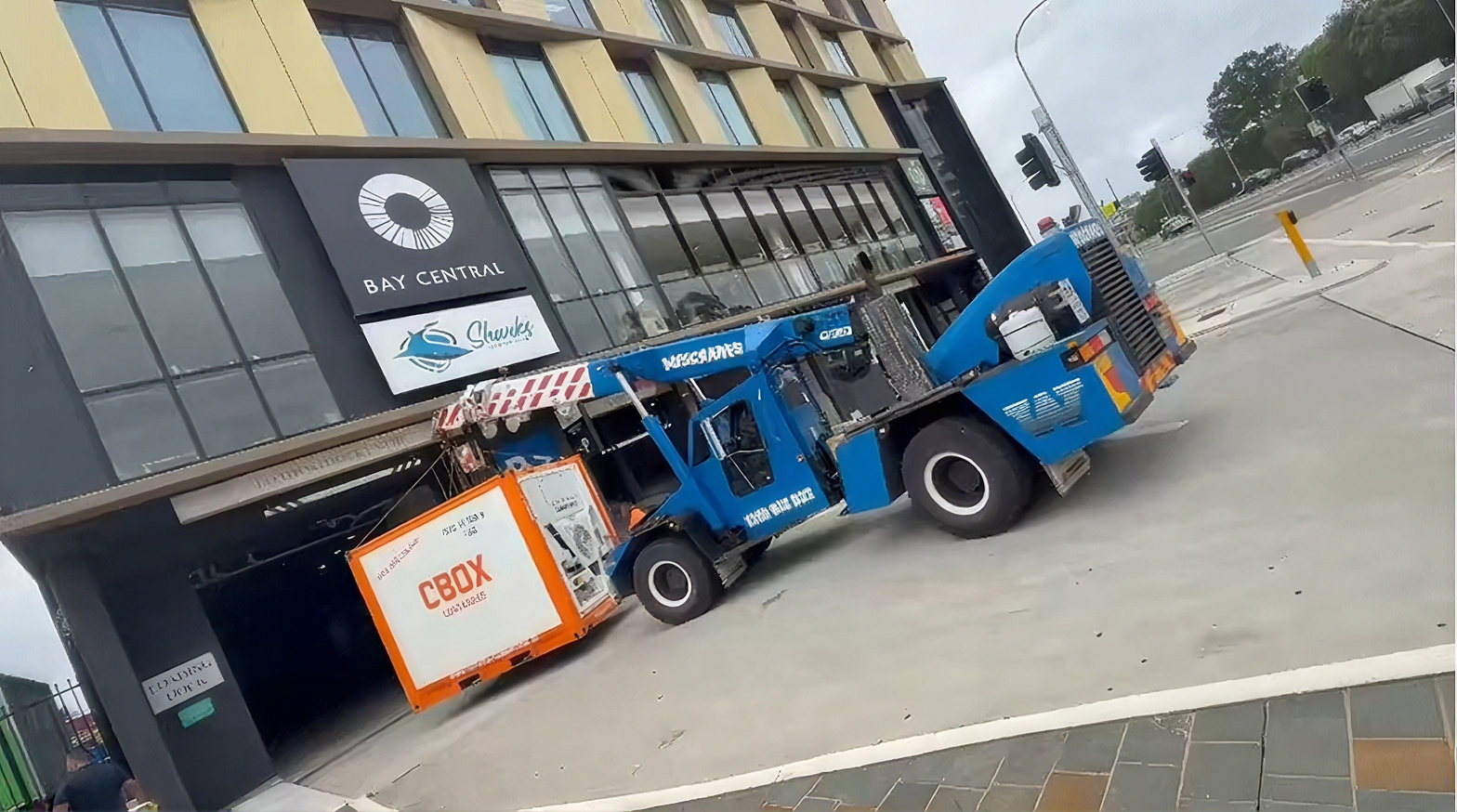 aWescranes Franna crane carrying a shipping container past a commercial building